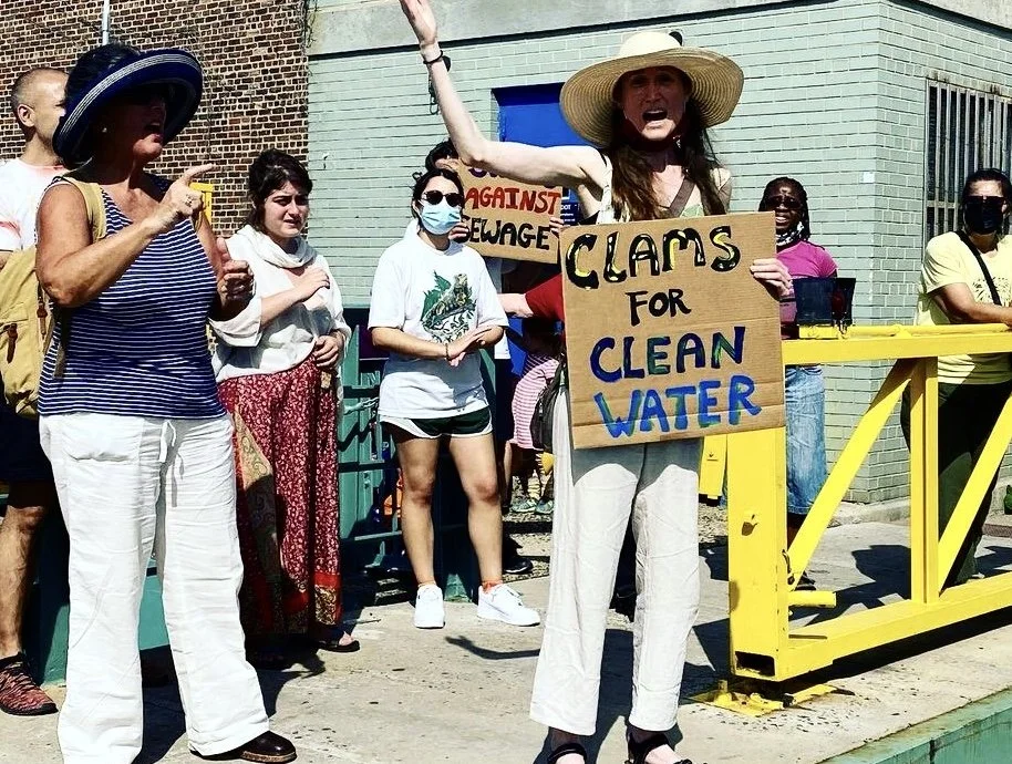 People in clam-themed costumes and protest signs on a bridge over or near the Gowanus Canal.