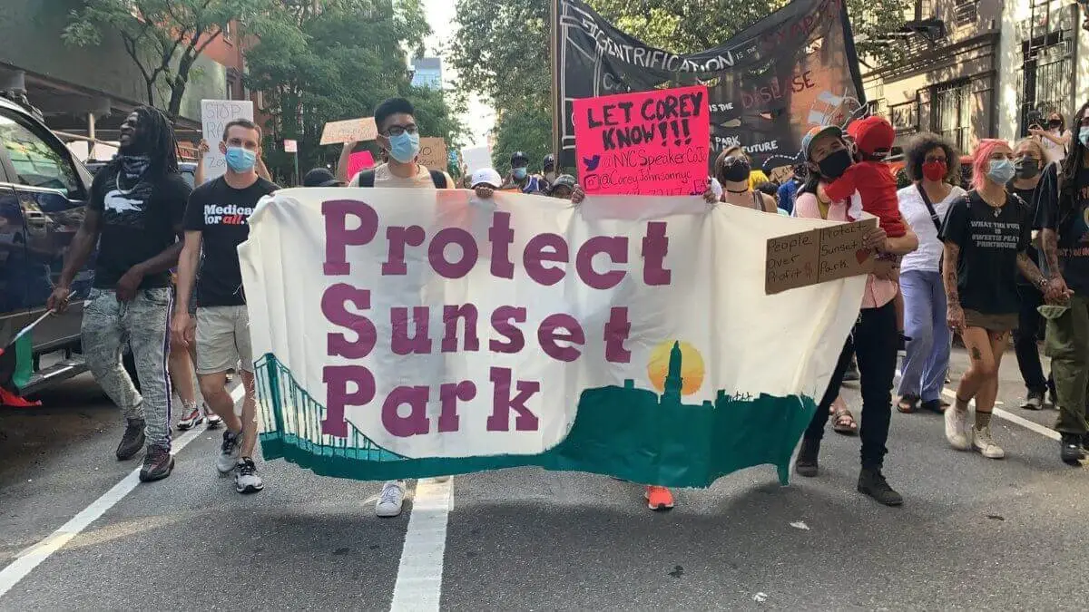Crowd of protesters with signs opposing Industry City rezoning outside a residential building.